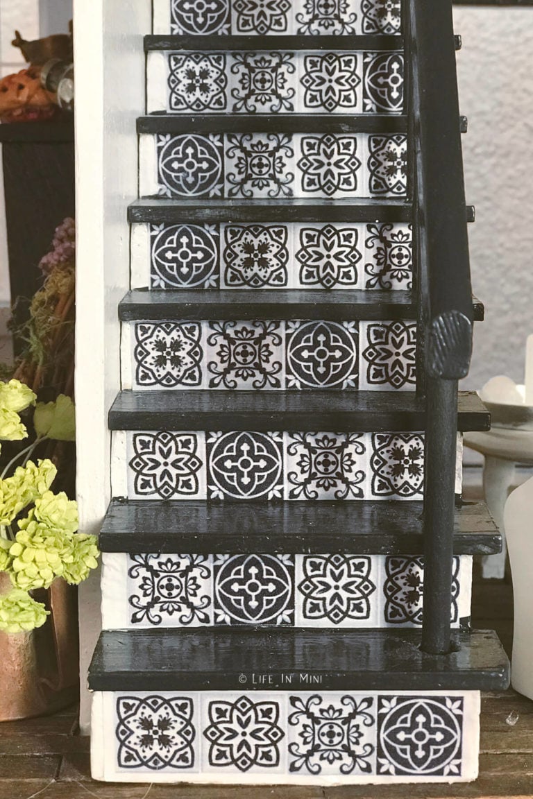 Closeup of dollhouse stairs painted white and black with Mexican talavera tile design