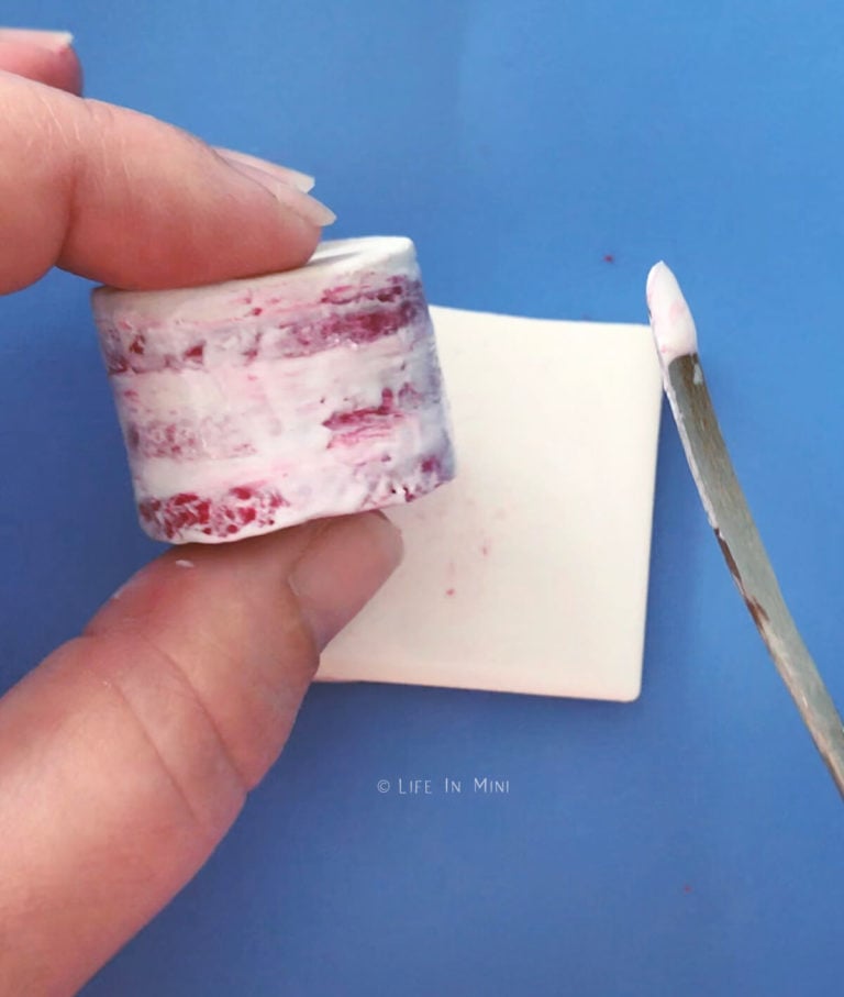 Adding white liquid polymer to the sides of a red miniature cake