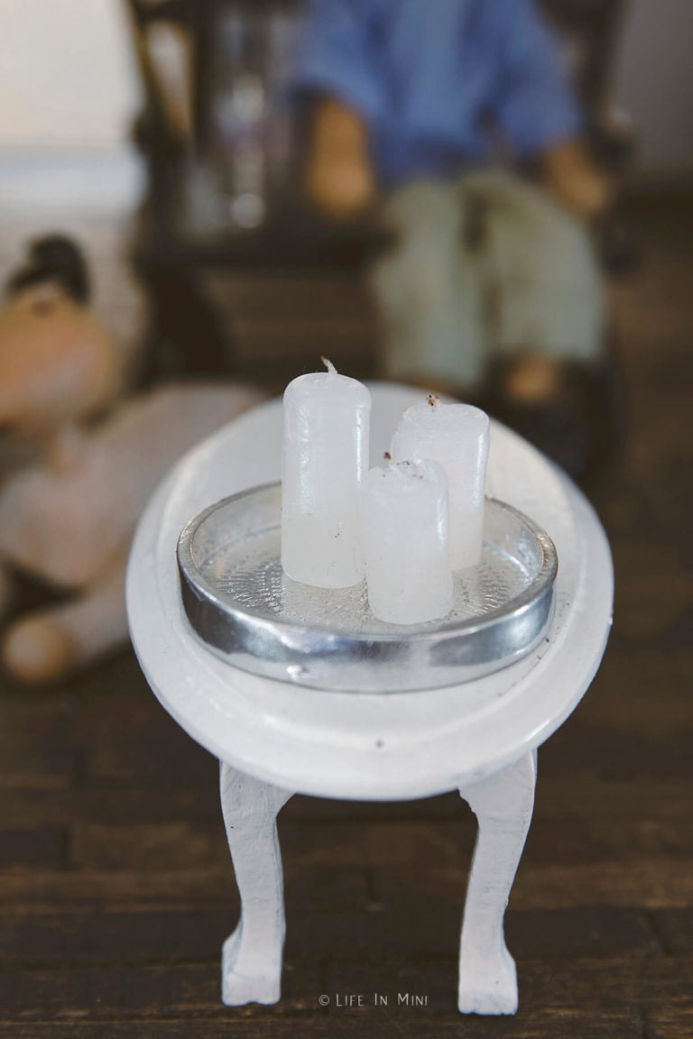 Miniature candles on a silver tray on a white coffee table inside a dollhouse