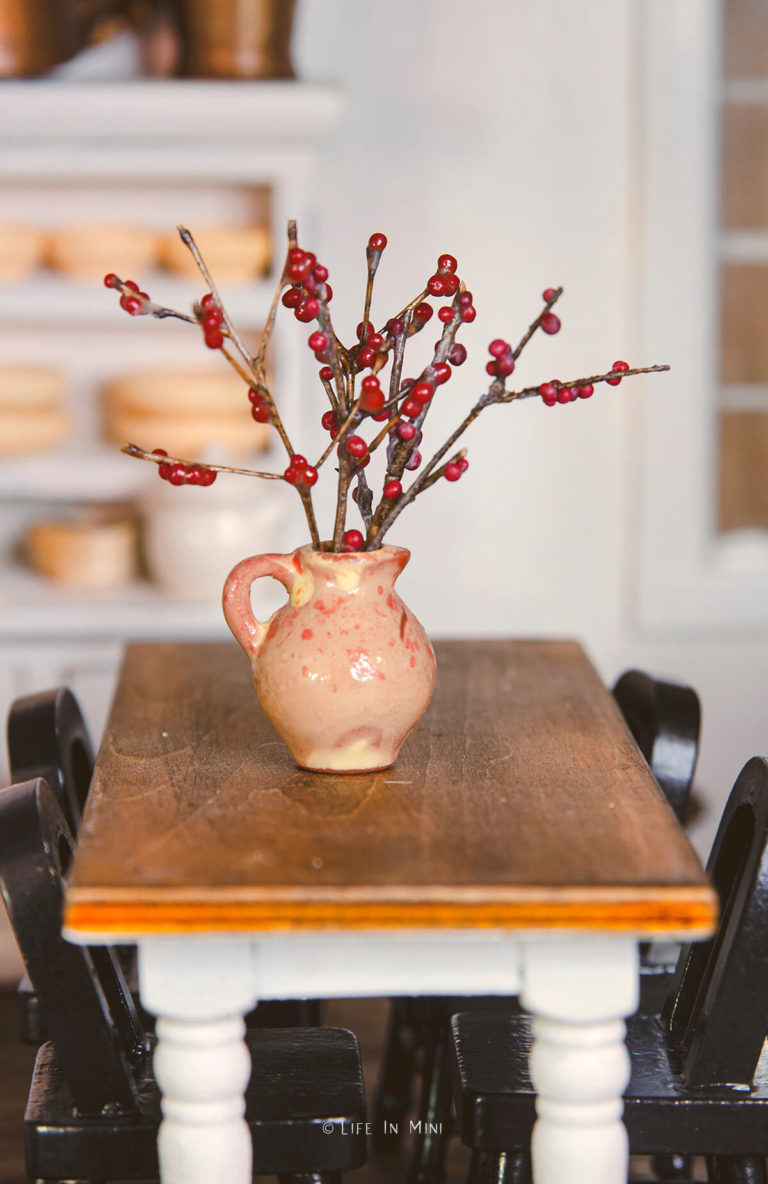 Miniature berry branches in a ceramic pitcher on a table in a dollhouse