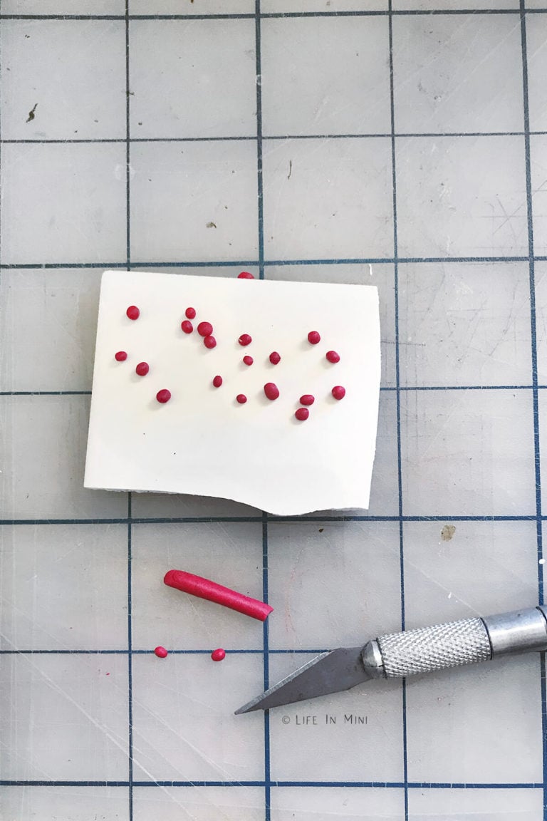 Rolling out tiny balls of red clay on a white tile