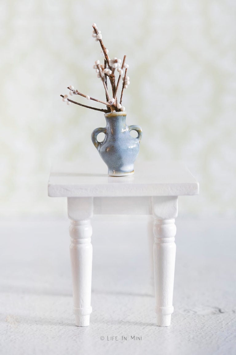Miniature white berry branches in a blue ceramic vase on a white table