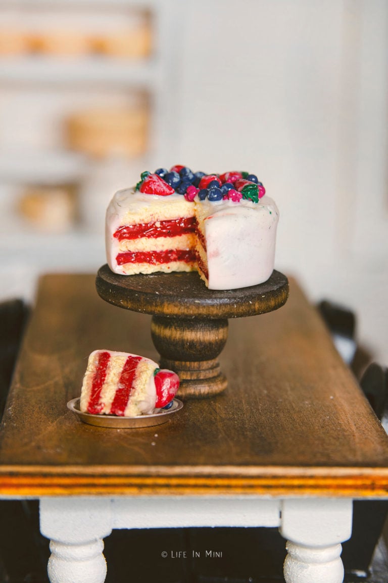 A miniature cake with berries on a mini wooden cake stand