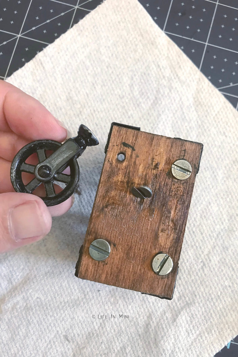 Screwing miniature pulley wheel to the base of a dollhouse coffee table
