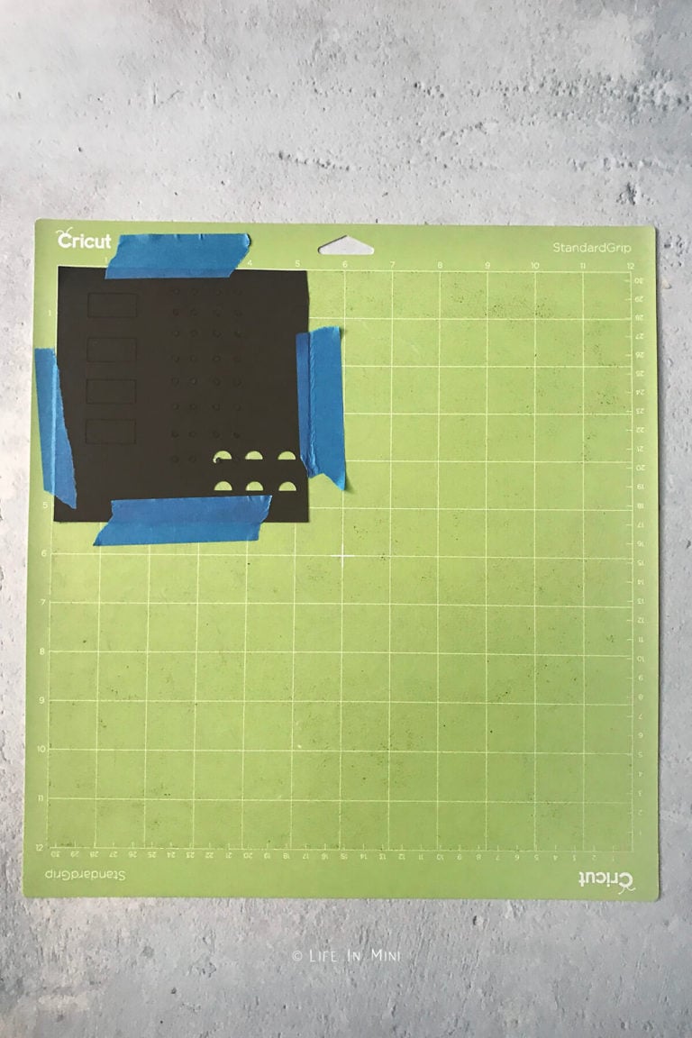 A small square piece of black kraftboard secured on a cricut mat