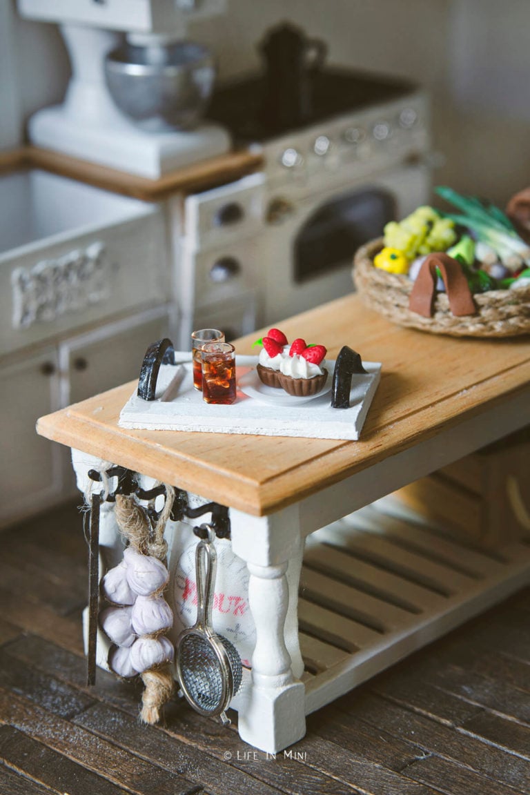 A white wood tray with drinks and cupcakes in a dollhouse kitchen