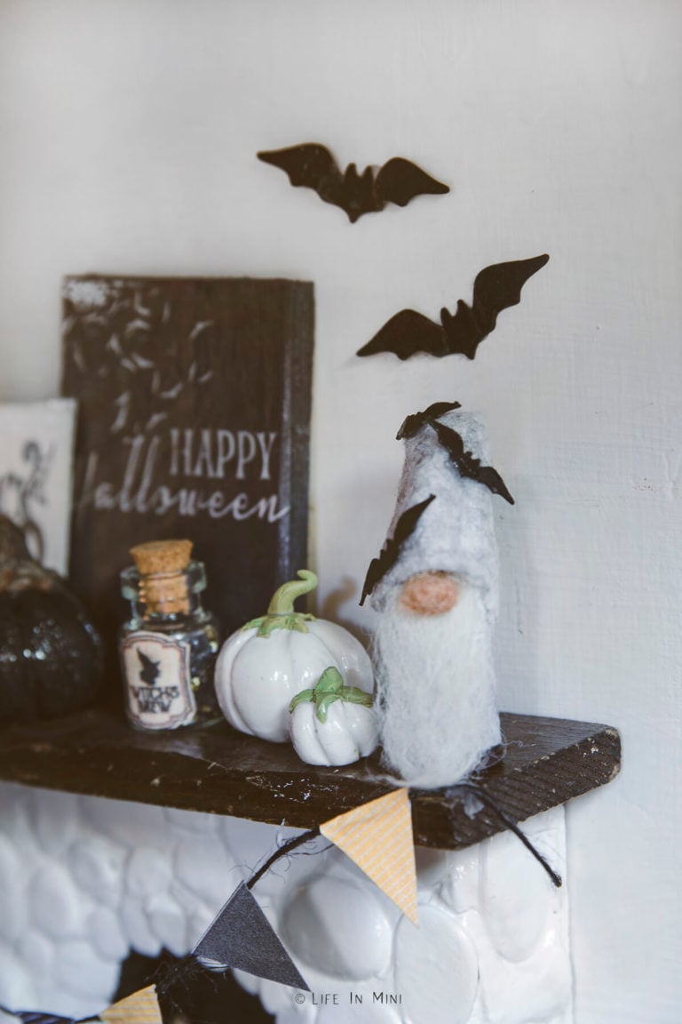 Closeup of a grey miniature gnome with bats on a dollhouse fireplace mantle with other halloween decorations