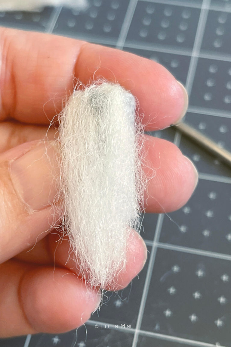 Gluing white felting wool onto form to make a miniature gnoome