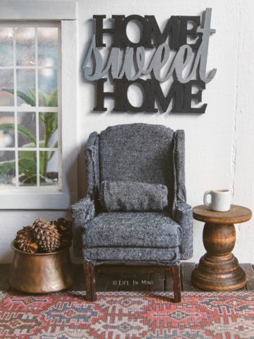 Miniature charcoal wing chair on a rug with a side table and a 'home sweet home' sign over it