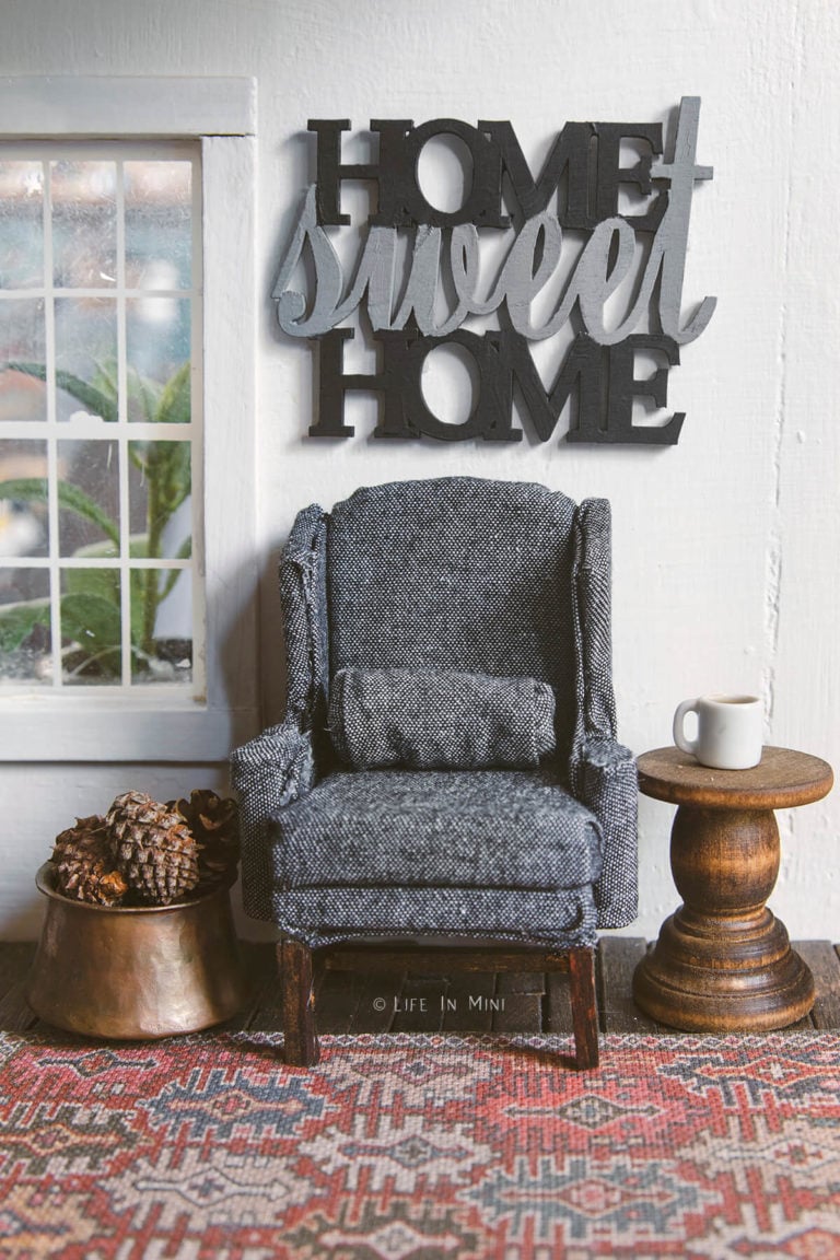 Miniature charcoal wing chair on a rug with a side table and a 'home sweet home' sign over it