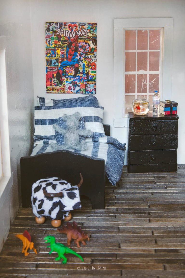 Dollhouse boy's bedroom with navy blue striped bedding, black wood bed frame and random toys