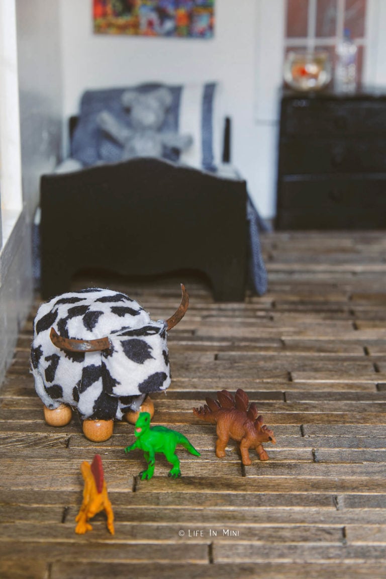 Dollhouse boy's bedroom with a cow ottoman and small dinosaur toys