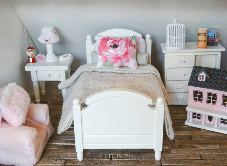 A dollhouse girl's bedroom with white wood bed frame with tan linen and dusty rose bedding and other furnishings