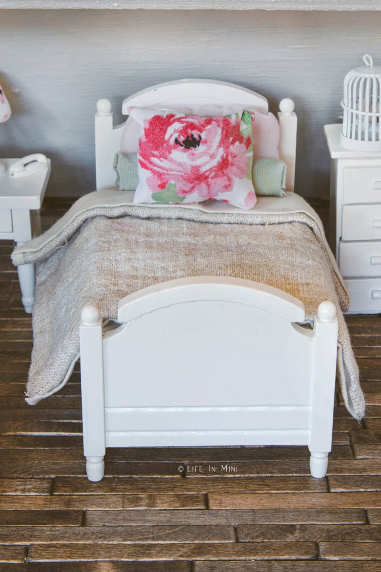 Closeup of a girl's bedroom with white wood bed frame with tan linen and dusty rose bedding