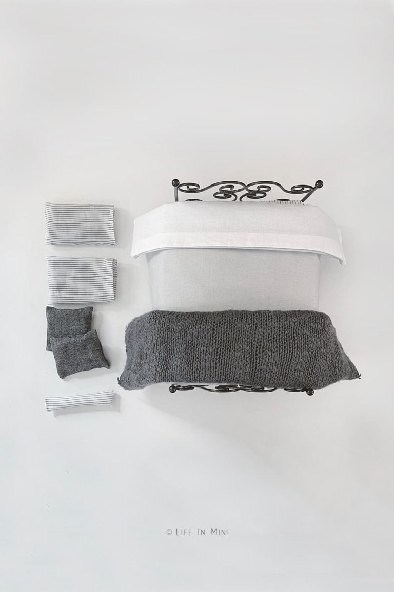 Overhead view of a black metal dollhouse bed with grey, charcoal and white bedding