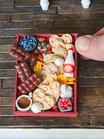 A hand holding a miniature valentine waffle board made of polymer clay, wood and resin