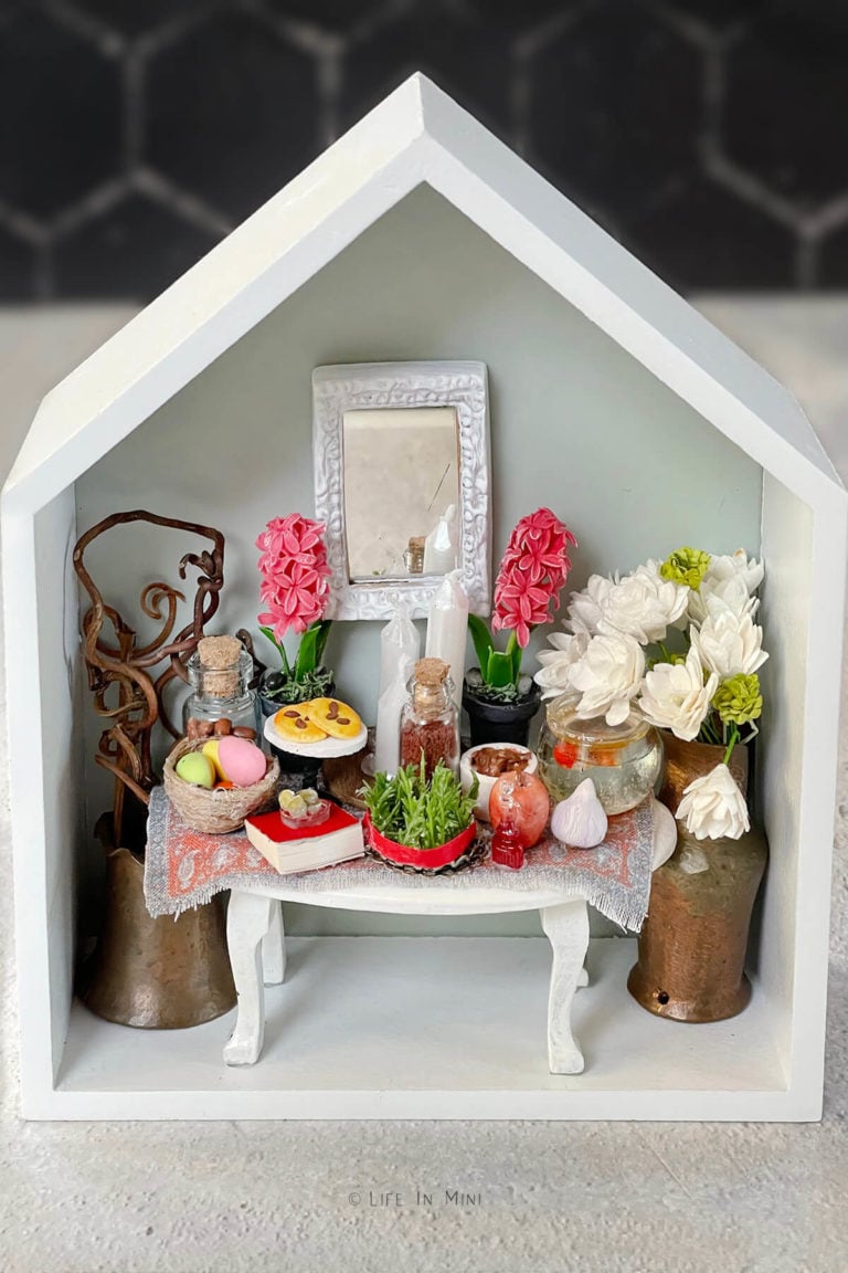 Closeup of a small house shaped box frame with a Persian New Year (Nowruz) table scape (haft sin) set in miniature
