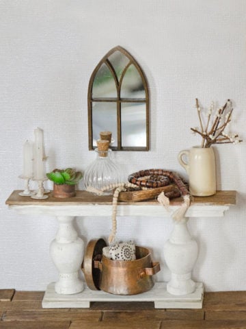 A miniature farmhouse console table with various dollhouse accessories on it
