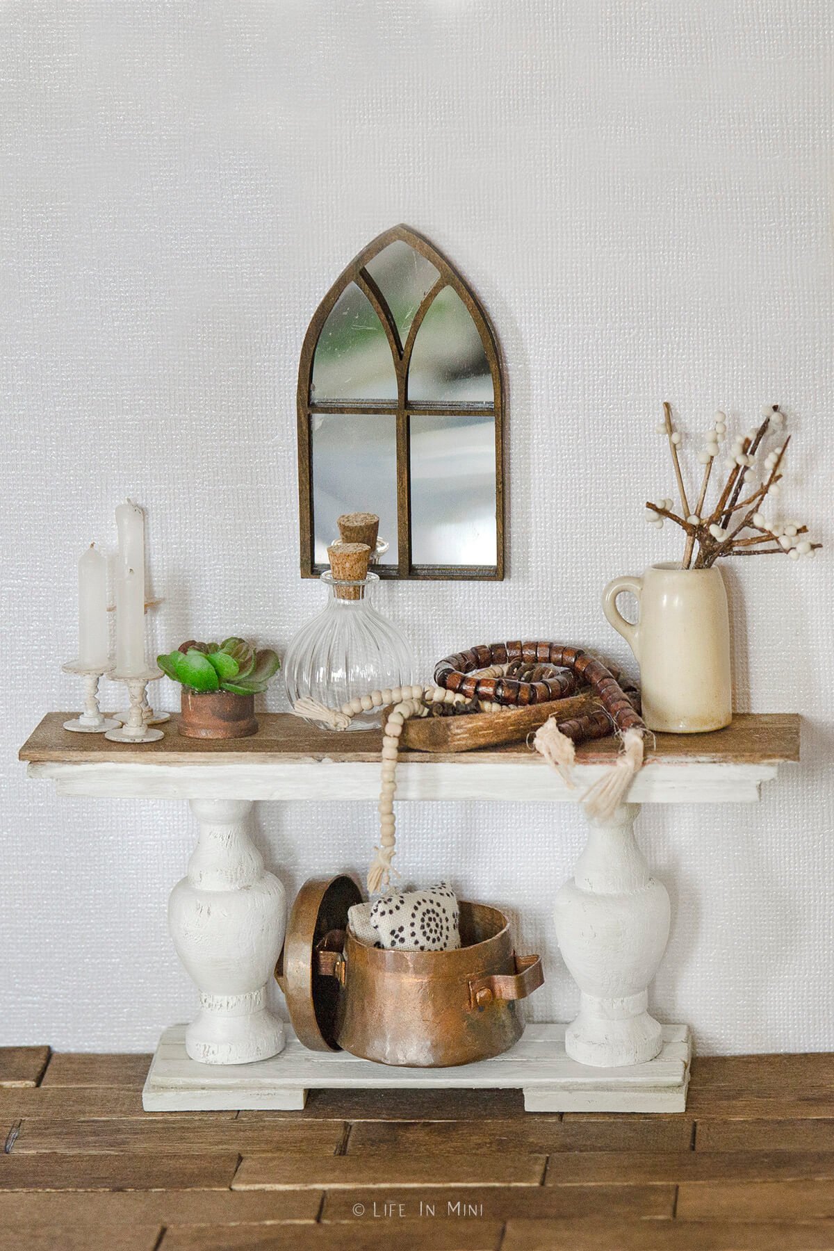 A miniature farmhouse console table with various dollhouse accessories on it