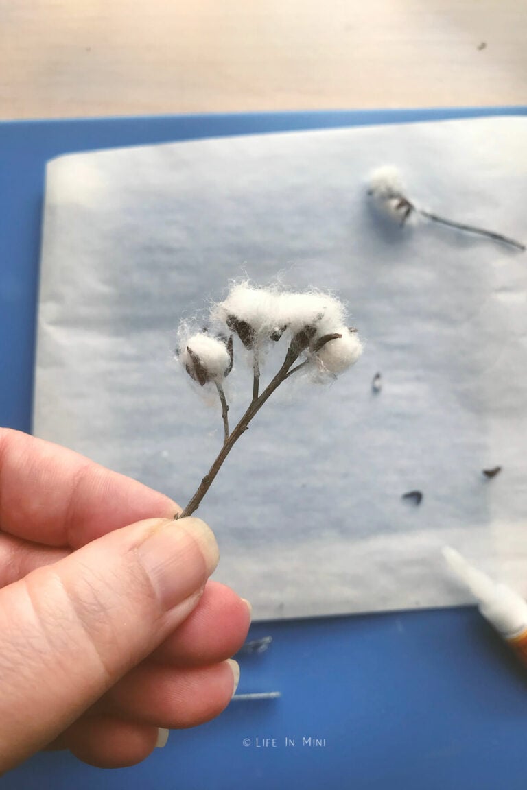 A hand holding a mini cotton stem with bits of brown clay glued onto it