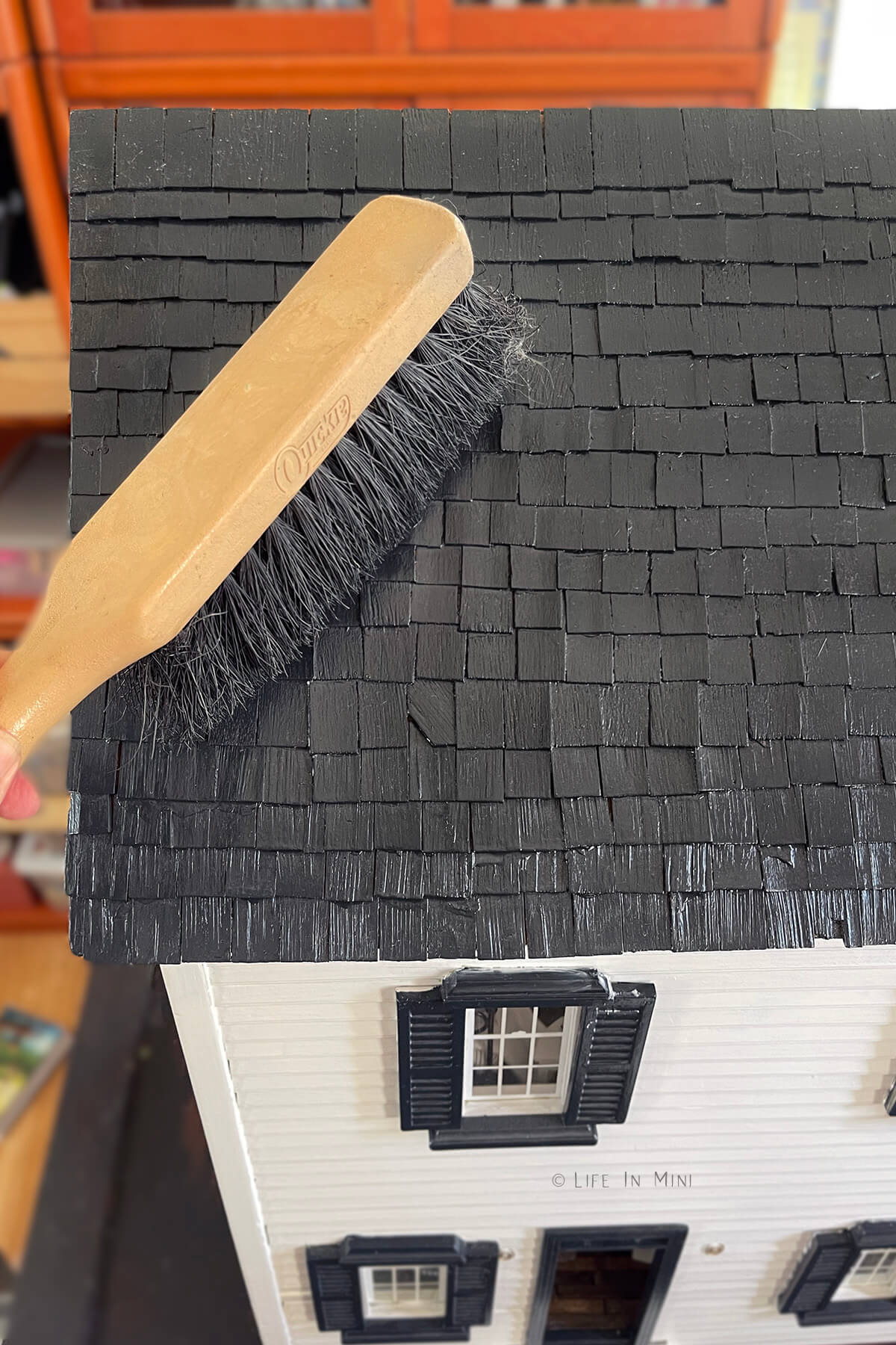 Brushing off dust and lint from a dollhouse roof