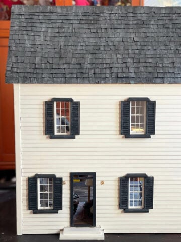 A white wood dollhouse with black trim and faux slate roof