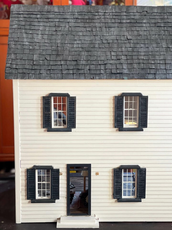 A white wood dollhouse with black trim and faux slate roof