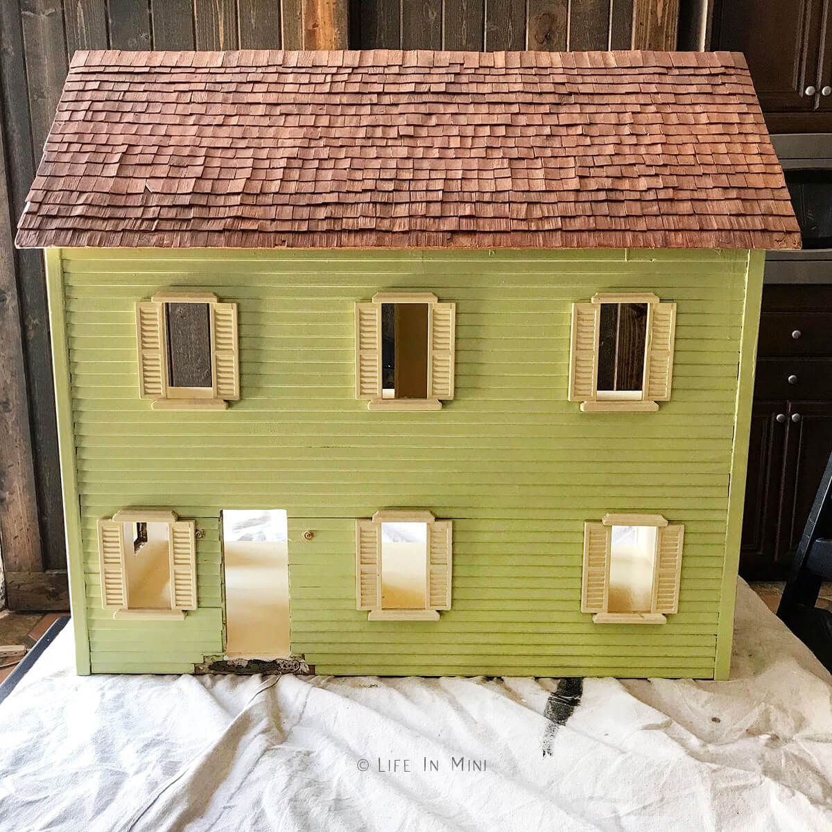 Green wood dollhouse with cream trim and natural wood shingle roof