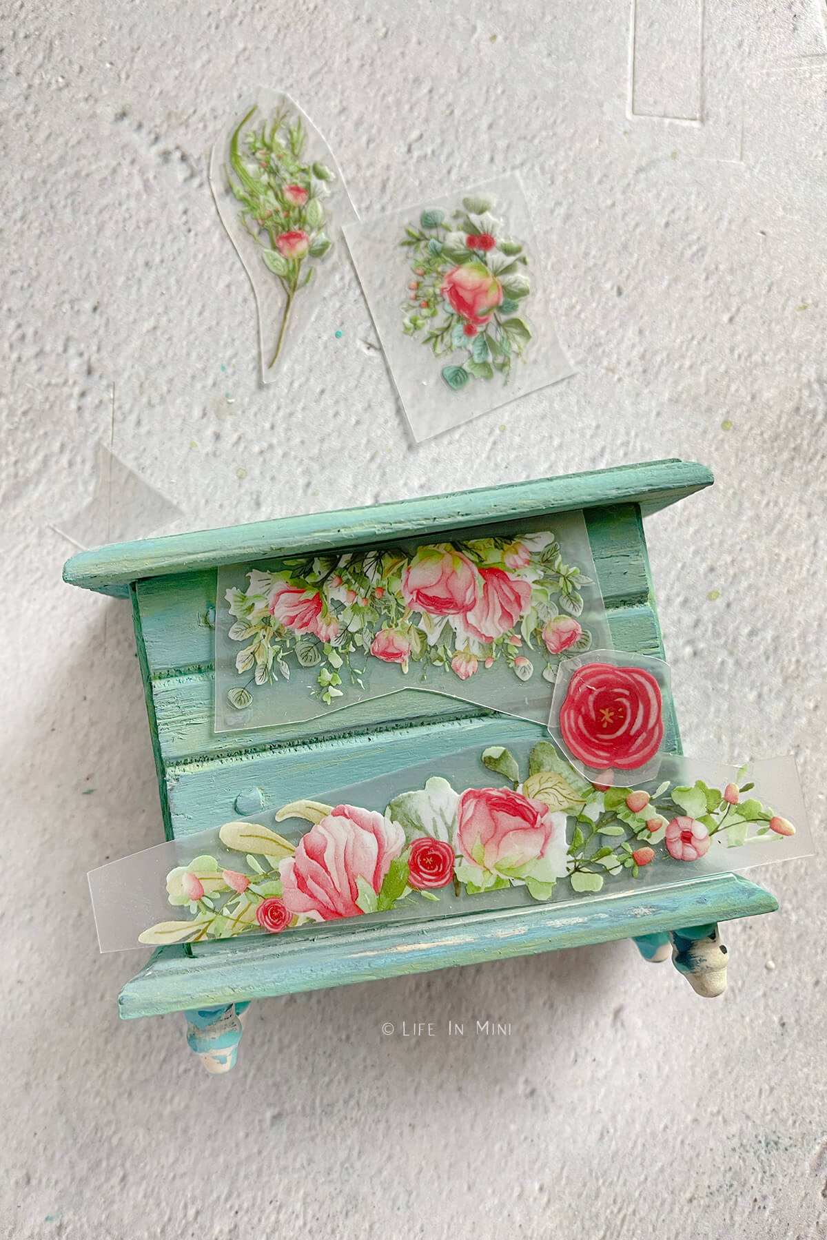 Arranging floral rub on transfers onto a teal dollhouse dresser