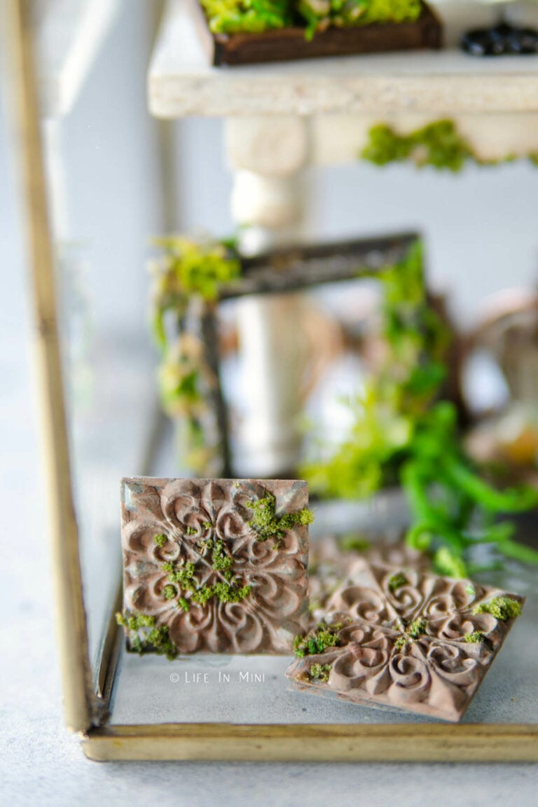 Closeup of two rustic miniature tiles with moss on it and mini garden accessories behind it