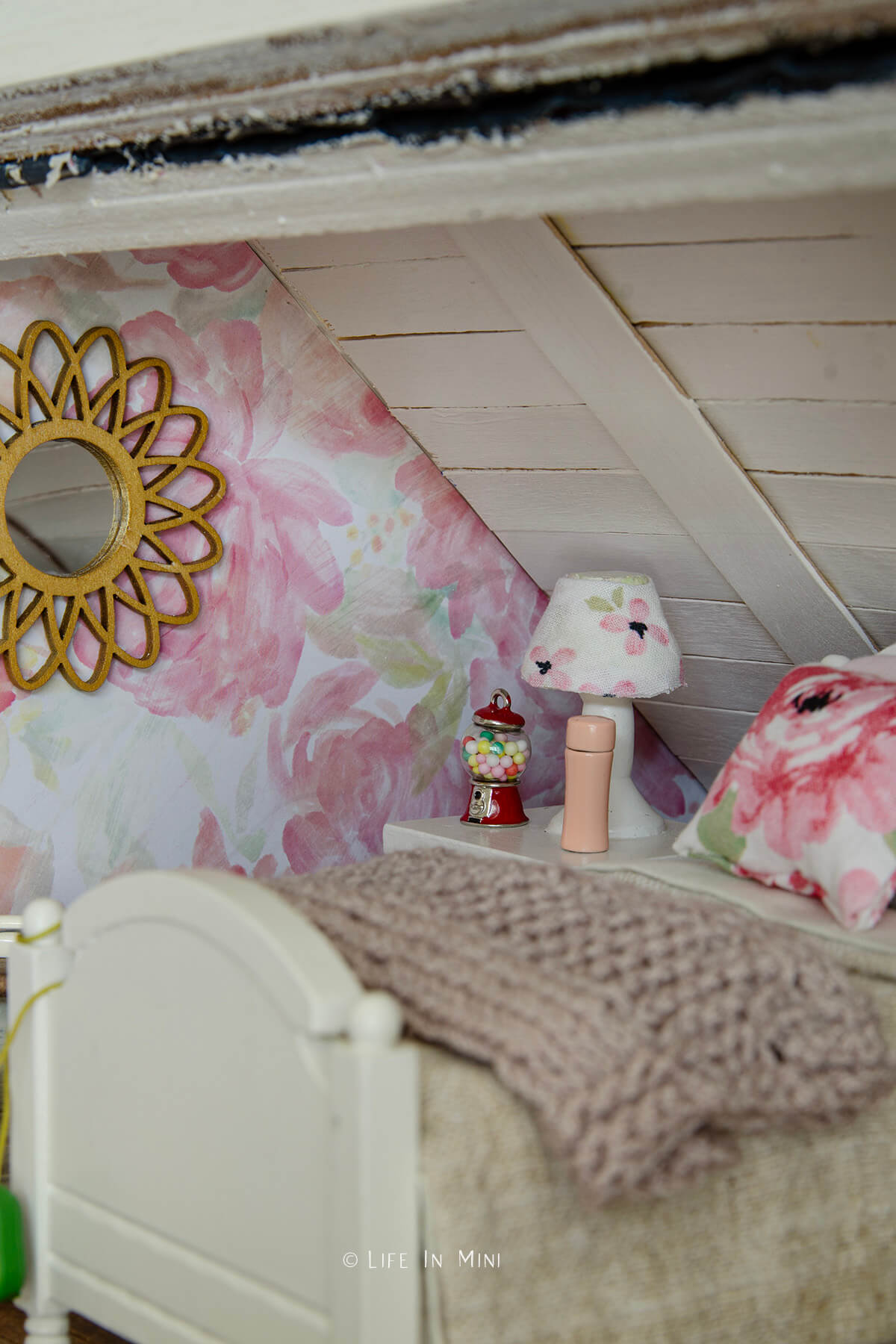 Closeup of a nightstand in a dollhouse bedroom with floral wall paper in the background