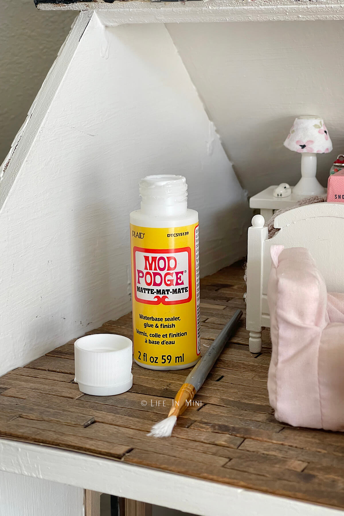 Closeup of a bottle of mod podge and a paint brush in a dollhouse attic