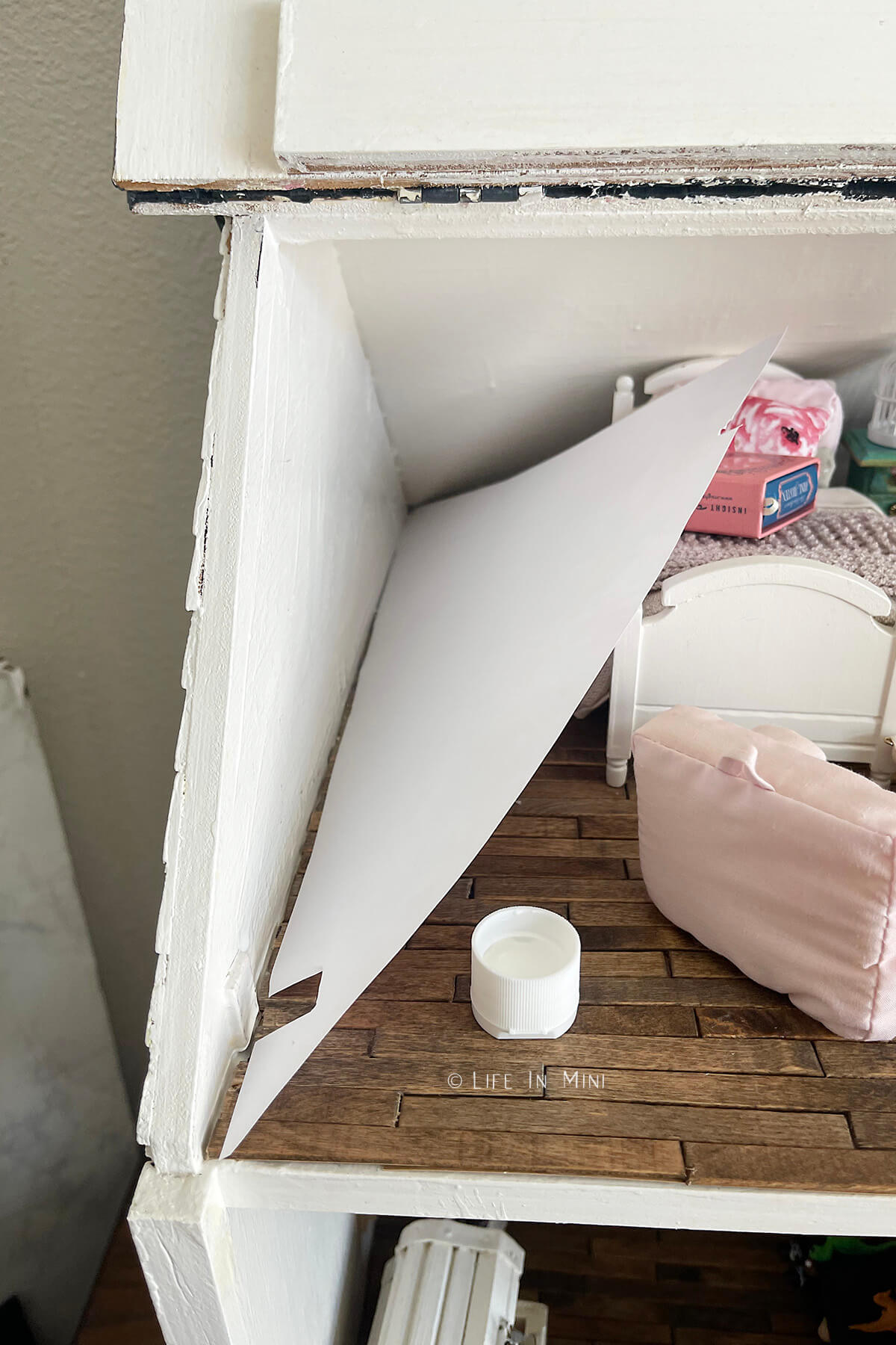 A triangular piece of dollhouse wall paper ready to be applied to a triangular wall in a dollhouse