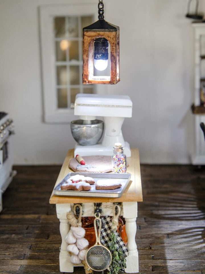 A miniature lantern pendant light lit and hanging in a dollhouse kitchen