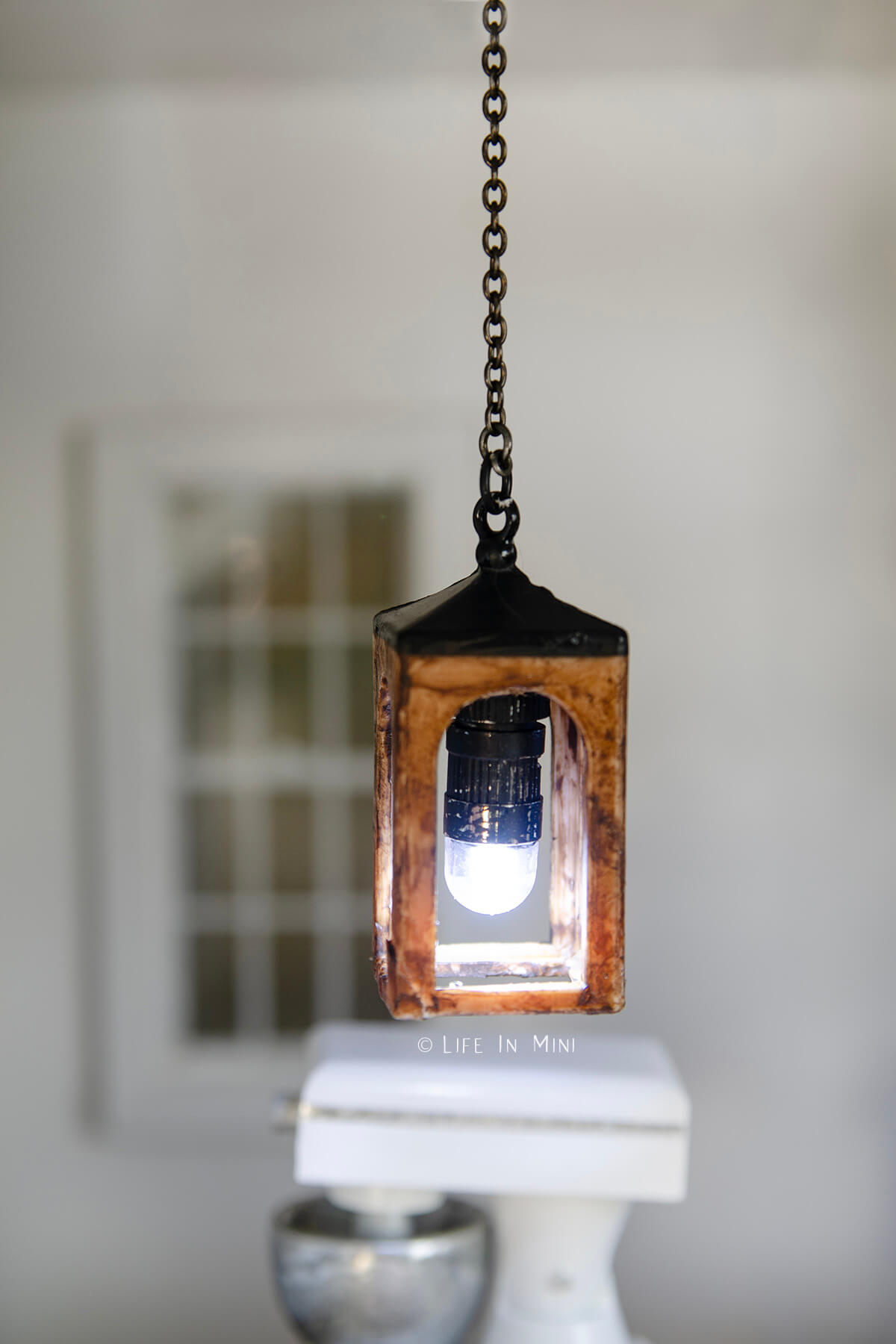 Closeup of a miniature lantern pendant light lit and hanging in a dollhouse
