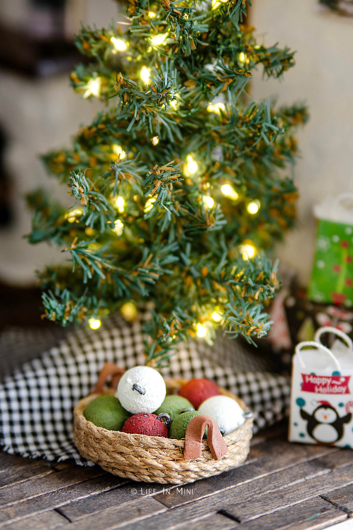 A dollhouse Christmas tree lit up with a basket of homemade chalk painted ornament balls in them