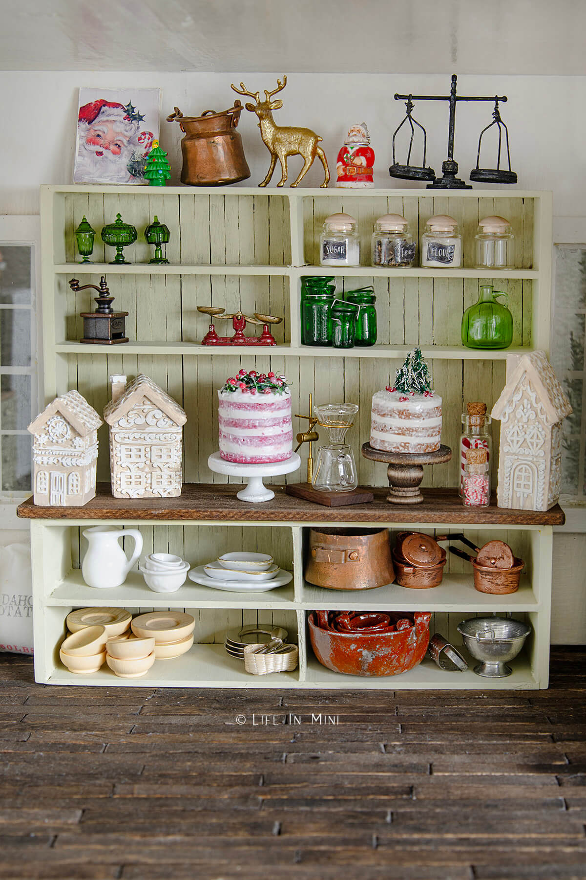 A large shelf unit in a dollhouse filled with Christmas cakes, gingerbread houses and kitchen stuff