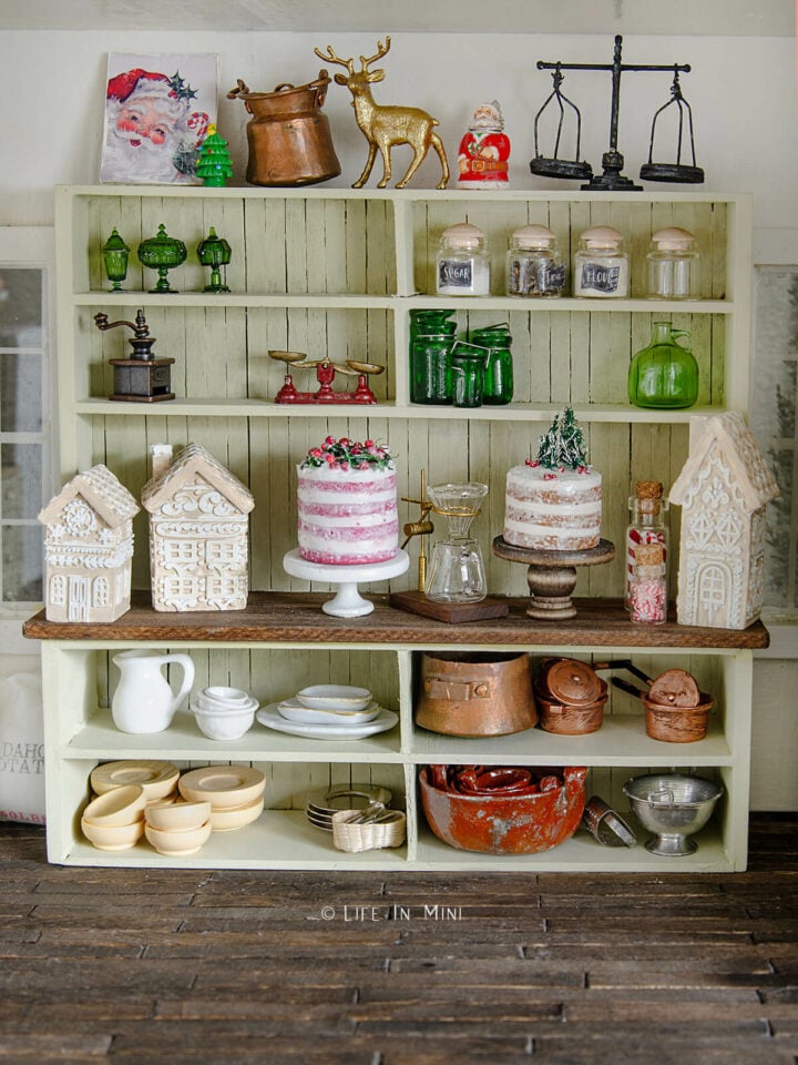 A large shelf unit in a dollhouse filled with Christmas cakes, gingerbread houses and kitchen stuff