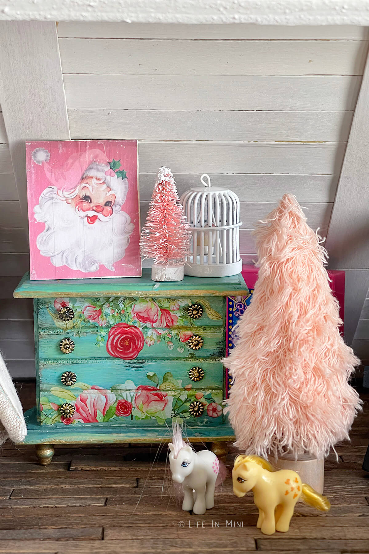 A floral decorated dollhouse dresser with a small pink Christmas tree and pink Santa artwork