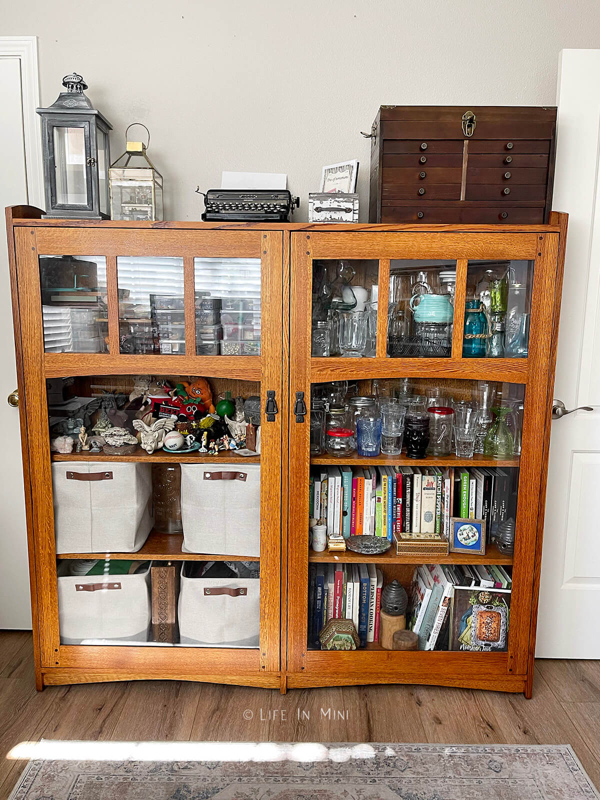 A wooden mission style cabinet with glass doors and art supplies organized in it