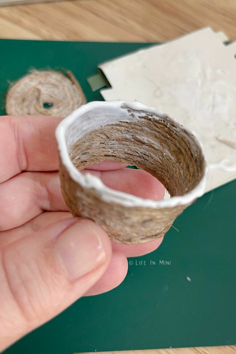 A hand holding a mini basket in the making with glue on it to fit the bottom