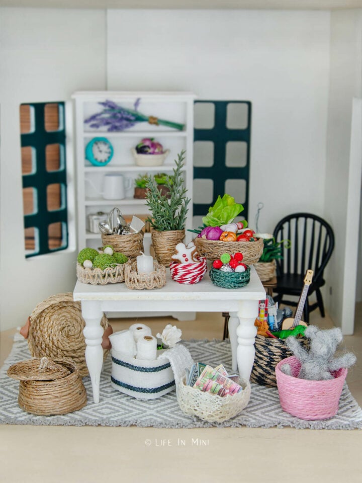 A dollhouse table with assorted mini baskets on it and around it filled with various accessories