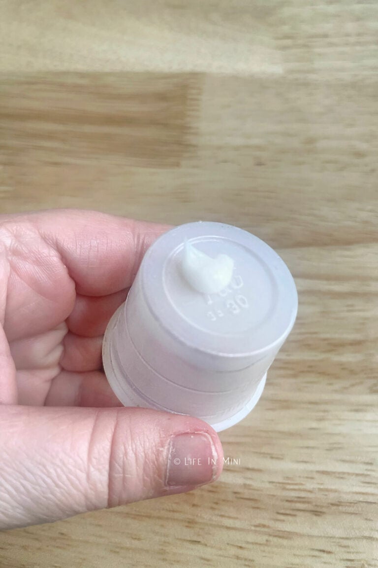 A hand holding a plastic medicine cup with a dab of hand lotion on it