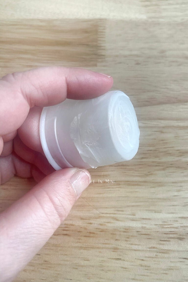 A hand holding a plastic medicine cup with hand lotion smeared all over it