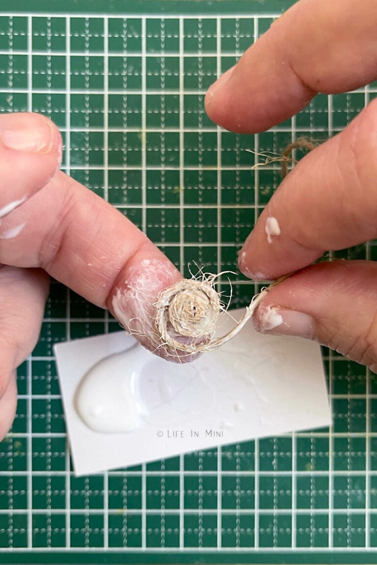 A hand making a small circle using white glue and twirling twine