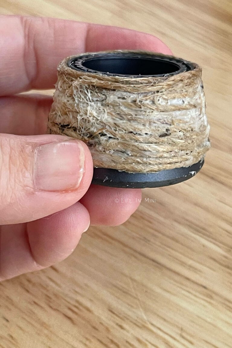 A hand holding a large plastic bottle cap with glue covered twine wrapped around it