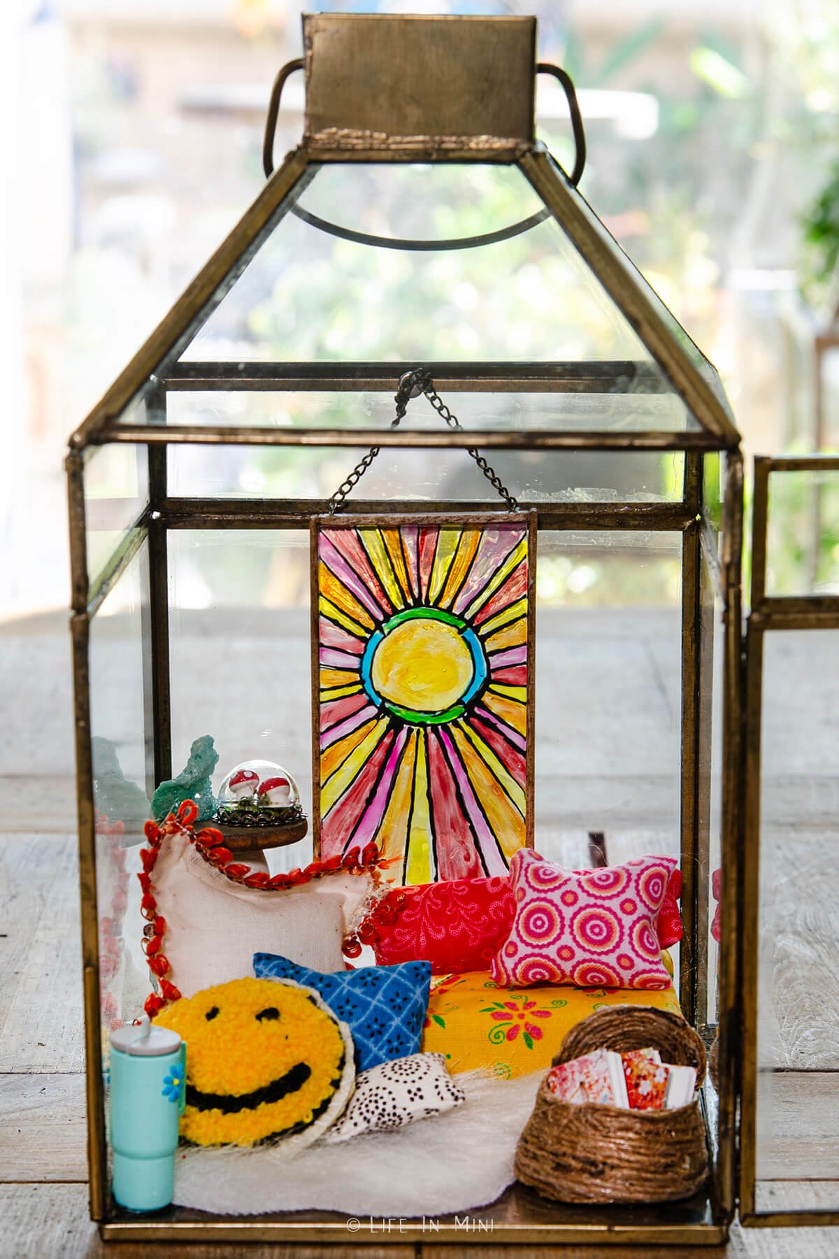 A miniature boho reading nook scene made in a lantern with colorful pillows and a sun design stained glass