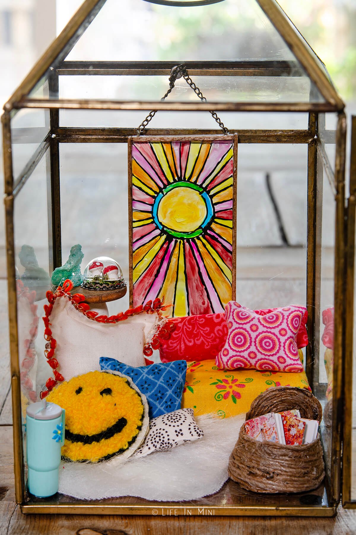 Closeup of a miniature boho reading nook scene made in a lantern with colorful pillows and a sun design stained glass