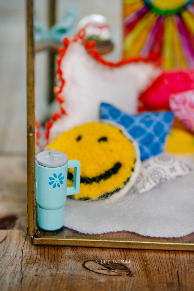 Closeup of a miniature Stanley mug with colorful pillows behind it in a miniature scene