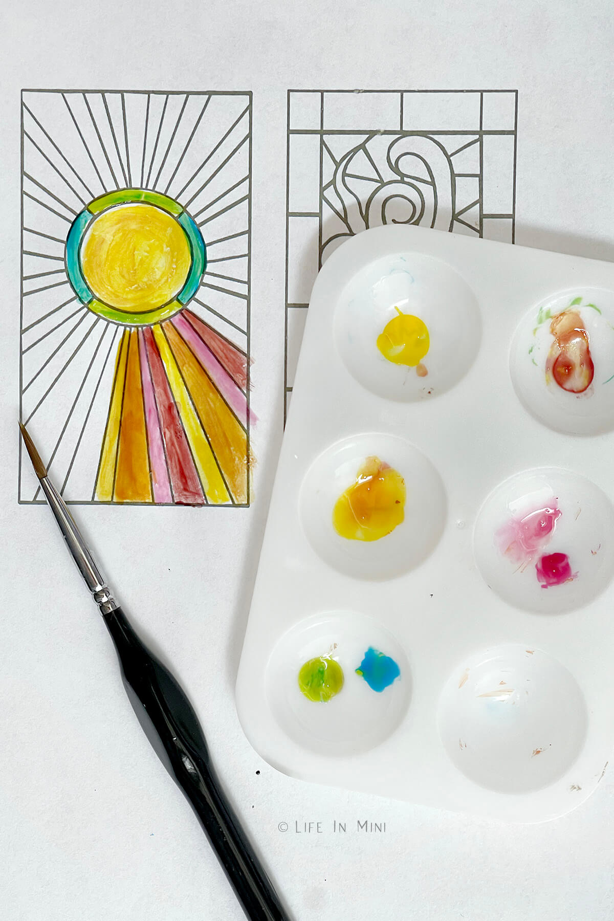 A piece of paper with a stained glass sun design on it with a paint brush starting to paint it for a color guide